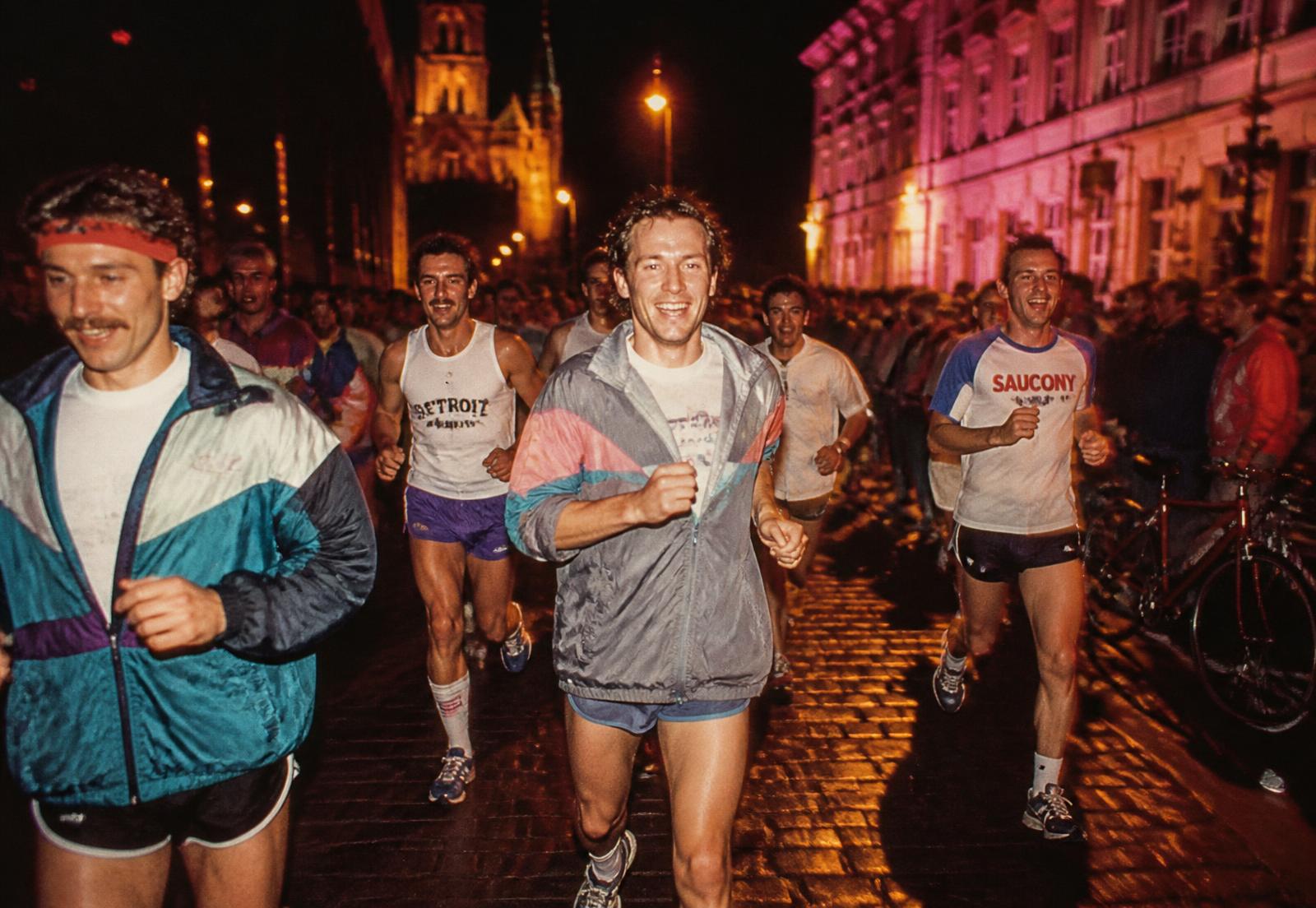 Lopers in retro sportkledij door Gent bij nacht